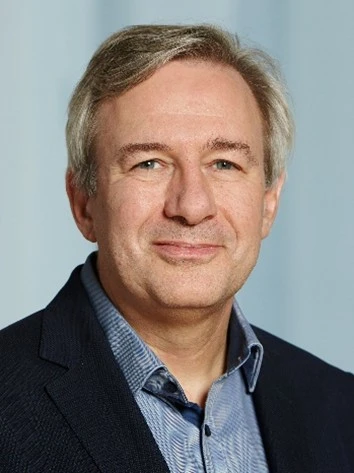 CLose up of Frank Schimmelfennig, wearing a dark suit jacket and a blue shirt, smiling at the camera